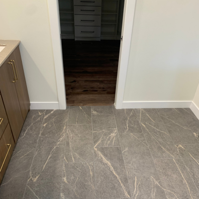Gray marble-pattern tile flooring with subtle white veining leads to an open doorway and a hallway with dark wood-look planks and white baseboards.